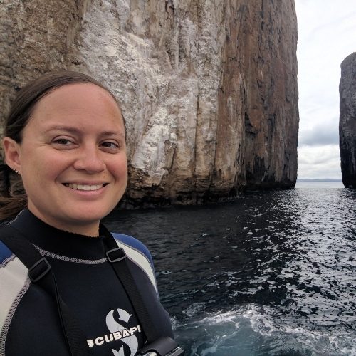 Katy on a boat wearing a wetsuit for snorkeling, in front of Kicker Rock in the Galapagos Islands